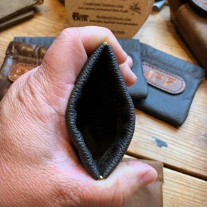Peut inclure: Une pochette en cuir marron fonc&eacute; avec des accents dor&eacute;s. La pochette est ouverte et l'int&eacute;rieur est visible. La pochette est faite de cuir souple et souple et a une finition lisse et polie.