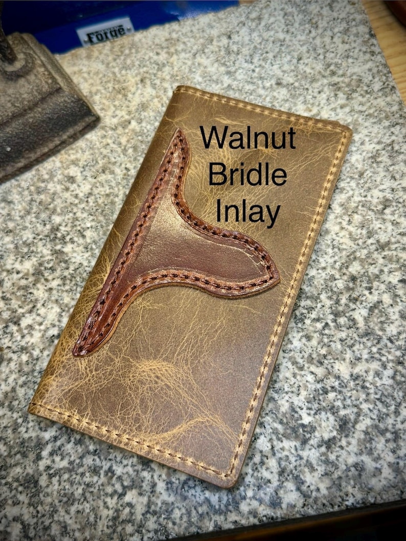 May include: A brown leather wallet with a walnut bridle inlay. The wallet has a stitched edge and a unique design.