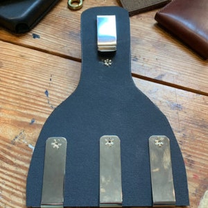 May include: A black leather wallet with three metal clips and a single metal clip on the top. The clips are secured with silver screws.