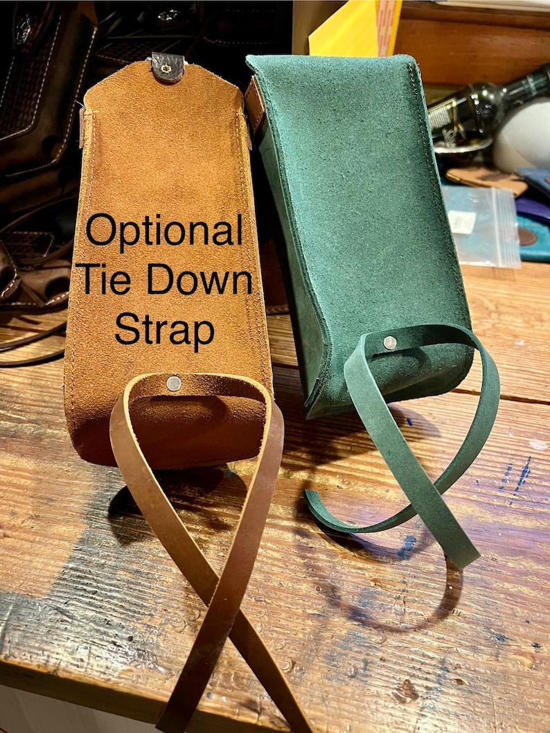 May include: Two leather pouches with optional tie down straps. The pouch on the left is brown and the pouch on the right is green.