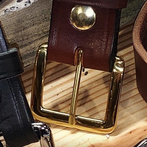 Peut inclure: Gros plan sur une ceinture en cuir marron avec une boucle dor&eacute;e. La boucle est de forme rectangulaire simple avec une finition lisse.