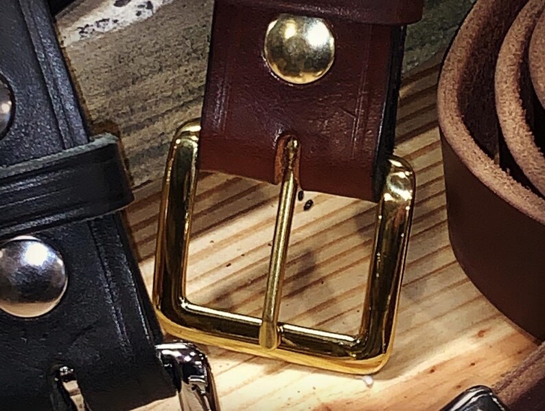 Peut inclure: Gros plan sur une ceinture en cuir marron avec une boucle dor&eacute;e. La boucle est de forme rectangulaire simple avec une finition lisse.