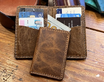 May include: A brown leather card holder wallet featuring a distressed texture and visible stitching. The wallet is open, revealing multiple interior slots filled with various credit cards, identification cards, and a folded one hundred dollar bill.