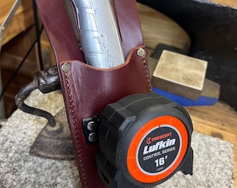 Puede incluir: Un cinturón de herramientas de cuero marrón con un cuchillo de uso general plateado y una cinta métrica roja y negra. La cinta métrica es una Lufkin Control Series 16' tape measure.