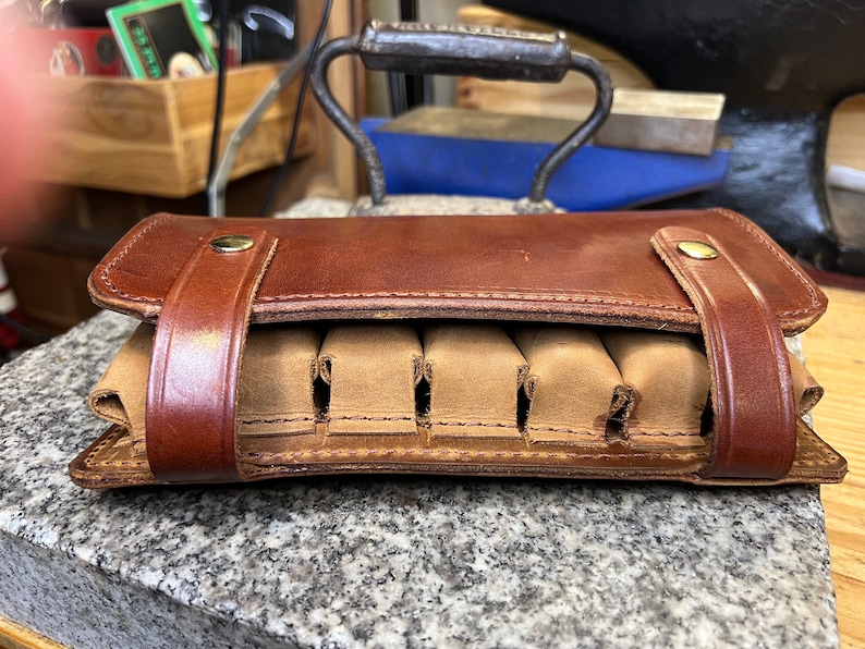 Puede incluir: Una funda de munici&oacute;n de cuero marr&oacute;n con seis ranuras para cartuchos. La funda tiene una solapa que se cierra con un broche.