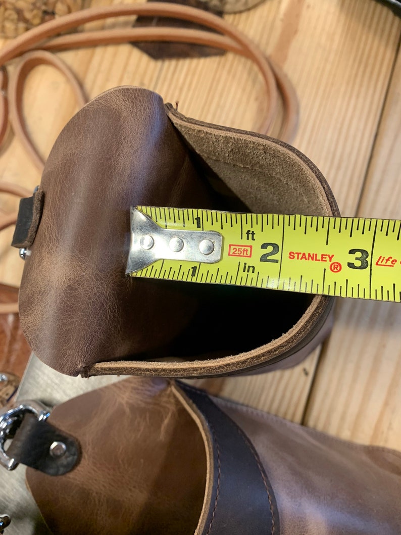 May include: A brown leather pouch with a yellow measuring tape inside. The tape reads "25ft" and "2 ft" with the Stanley logo visible. The pouch is open and the tape is measuring the inside of the pouch.