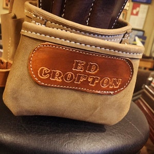 May include: A brown leather tool belt with a brown leather patch that says "ED CROFTON" in white lettering.