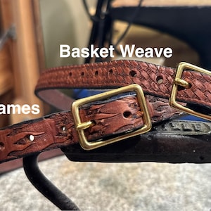 May include: Close-up of two brown leather belts with brass buckles. One belt features a basket weave pattern, while the other has a flame design. The word "Flames" is visible on one belt.