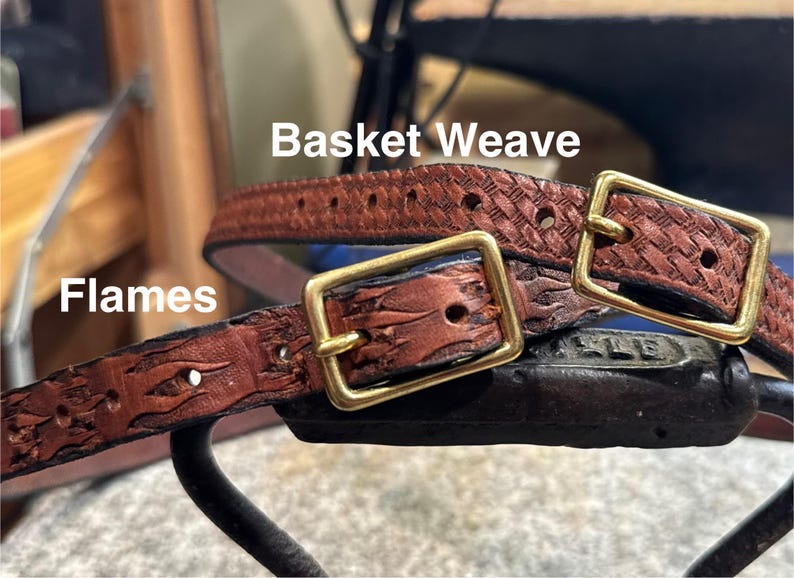 May include: Close-up of two brown leather belts with brass buckles. One belt features a basket weave pattern, while the other has a flame design. The word "Flames" is visible on one belt.