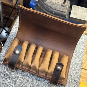 Puede incluir: Una funda de munici&oacute;n de cuero marr&oacute;n con ocho ranuras para cartuchos. La funda tiene una solapa que se cierra con un broche. La funda est&aacute; hecha de cuero grueso y duradero y tiene un aspecto r&uacute;stico.