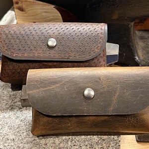May include: Two brown leather pouches with metal snaps. The top pouch has a textured design. The bottom pouch has a smooth surface.