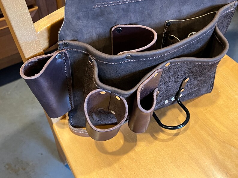 May include: A brown leather tool belt with multiple pockets and a metal loop. The belt has a worn, distressed look.