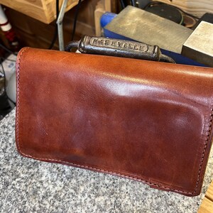 Puede incluir: Una cartera de cuero marr&oacute;n con un asa de metal que dice "Nashville".