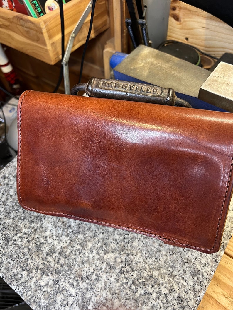 Puede incluir: Una cartera de cuero marr&oacute;n con un asa de metal que dice "Nashville".