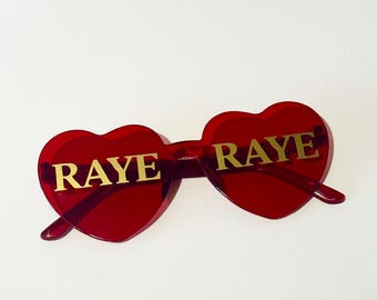 RAYE tour 2026 merchandise concert sunglasses red and gold