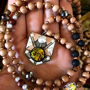 May include: A wooden beaded necklace with a geometric pendant featuring a green iridescent stone and white pearls. The necklace is made with brown, white, and black beads.