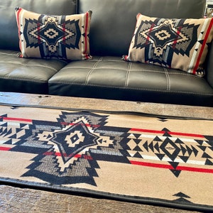 Puede incluir: Un sofá de cuero negro con dos almohadas estampadas y una manta de tiro estampada en marrón y negro sobre una mesa de café de madera.