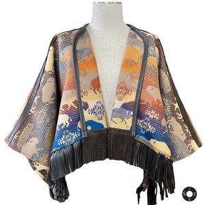May include: A brown, blue, and orange patterned poncho with fringe trim. The poncho is made of a soft, woven fabric and features a geometric design with images of buffalo.