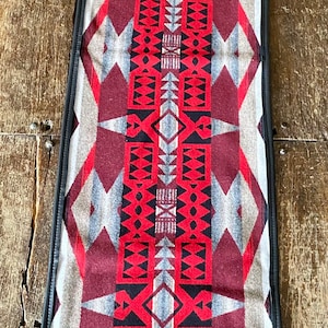 May include: A long, rectangular table runner with a black border and a geometric pattern in shades of red, black, gray, and white.