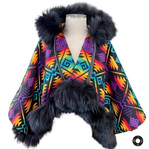 May include: A colorful poncho with a geometric pattern in shades of red, orange, yellow, green, blue, and purple. The poncho has a black fur-lined hood and trim. The garment is displayed on a mannequin.