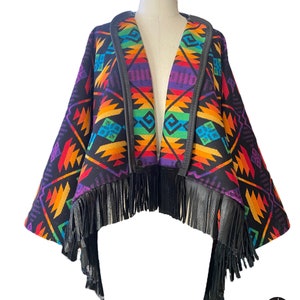 May include: A black and rainbow patterned poncho with leather trim and fringe. The poncho has a geometric design with a rainbow color scheme.