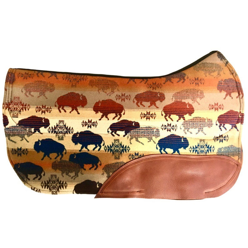 May include: A brown and tan saddle pad with a repeating pattern of blue and brown buffalo silhouettes. The saddle pad has a brown leather flap on the bottom right corner.