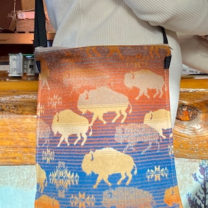 Puede incluir: Un bolso bandolera azul y naranja con un patrón de búfalo. El bolso está hecho de tela tejida y tiene un cierre de cremallera.