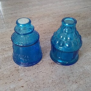 Peut inclure: Deux bouteilles en verre bleu avec des motifs d&eacute;coratifs. La bouteille de gauche a un motif textur&eacute; et la bouteille de droite a un motif &agrave; bulles.