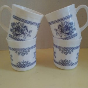 May include: Set of four white ceramic mugs with blue floral and geometric designs. The mugs have a handle and are stacked in pairs.
