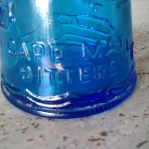 Peut inclure: Une bouteille en verre bleu avec les mots "Cape May Bitters" en relief sur le c&ocirc;t&eacute;.