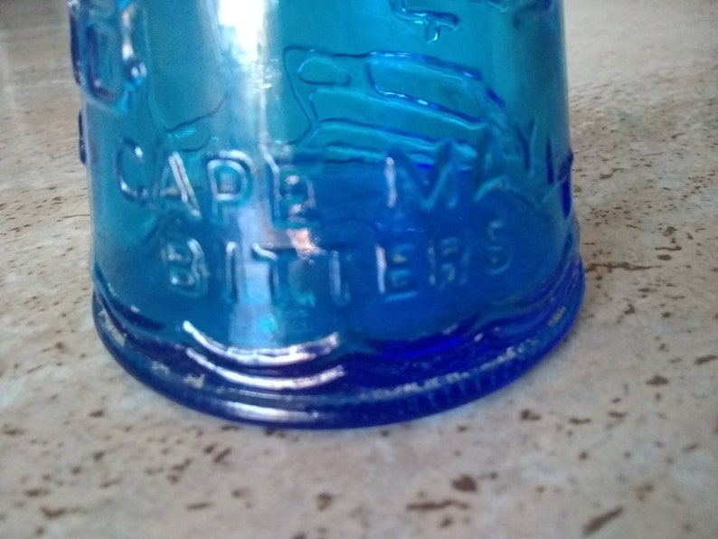 Peut inclure: Une bouteille en verre bleu avec les mots "Cape May Bitters" en relief sur le c&ocirc;t&eacute;.