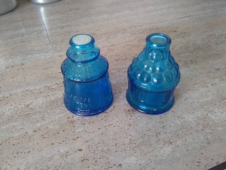 Peut inclure: Deux bouteilles en verre bleu avec des motifs d&eacute;coratifs. La bouteille de gauche a un motif textur&eacute; et la bouteille de droite a un motif &agrave; bulles.