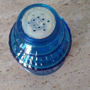Peut inclure: Un saupoudreur en verre bleu avec un couvercle en plastique blanc et un motif de trous ronds pour saupoudrer le sel.