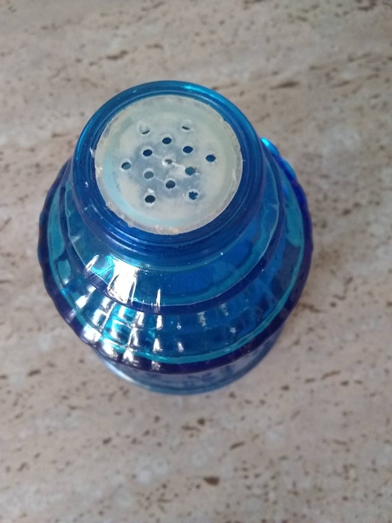 Peut inclure: Un saupoudreur en verre bleu avec un couvercle en plastique blanc et un motif de trous ronds pour saupoudrer le sel.