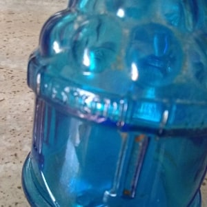 Peut inclure: Une bouteille en verre bleu avec une surface textur&eacute;e et un design d&eacute;coratif. La bouteille a une large ouverture et un goulot &eacute;troit.