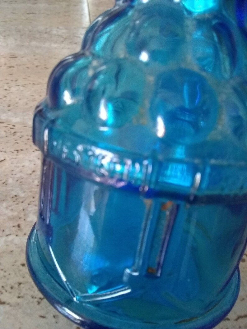 Peut inclure: Une bouteille en verre bleu avec une surface textur&eacute;e et un design d&eacute;coratif. La bouteille a une large ouverture et un goulot &eacute;troit.