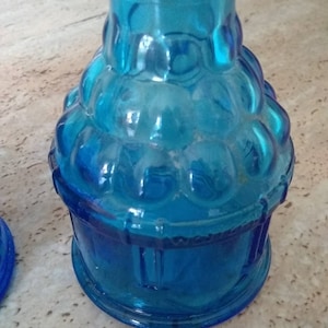 Peut inclure: Une bouteille en verre bleu avec un design textur&eacute; et bulbeux. La bouteille a une base ronde et un col &eacute;troit.