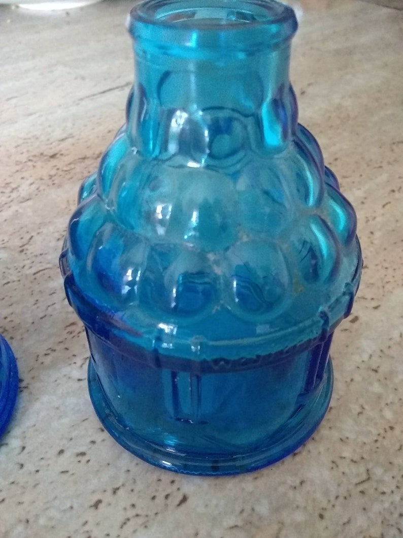 Peut inclure: Une bouteille en verre bleu avec un design textur&eacute; et bulbeux. La bouteille a une base ronde et un col &eacute;troit.