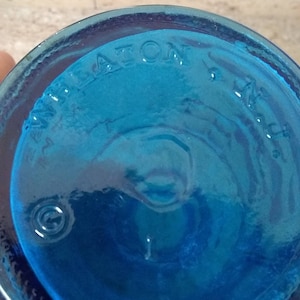 Peut inclure: Gros plan du fond d'une bouteille en verre bleu avec le mot "WHEATON" en relief au fond.