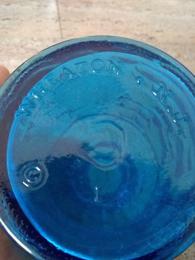 Peut inclure: Gros plan du fond d'une bouteille en verre bleu avec le mot "WHEATON" en relief au fond.