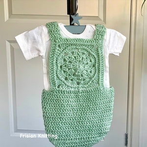 May include: A light green crocheted baby romper with a square-shaped design featuring a circular pattern in the center. The romper is on a white background.