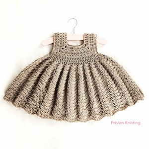 May include: A crocheted brown sleeveless dress with a scalloped hem, hanging on a pink hanger. The dress has a simple design with a small, open neckline. The text "Frisian Knitting" is visible in the bottom right corner of the image.