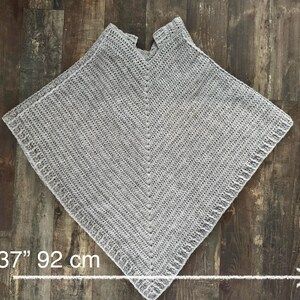 K&ouml;nnte beinhalten: Ein graues H&auml;kelponcho mit V-Ausschnitt. Das Poncho ist 85 cm lang und 92 cm breit. L: 33" 85 cm W: 37" 92 cm