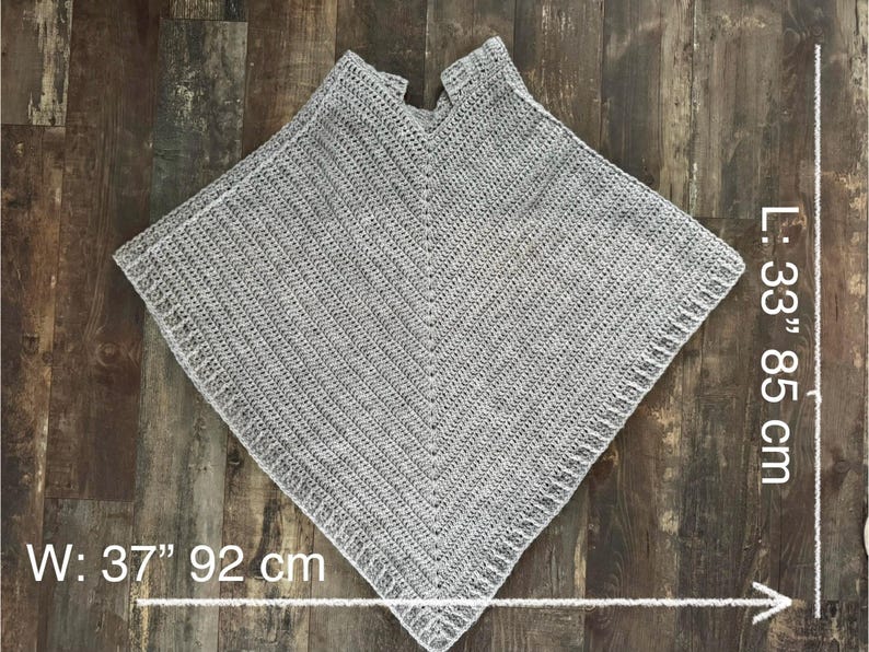 K&ouml;nnte beinhalten: Ein graues H&auml;kelponcho mit V-Ausschnitt. Das Poncho ist 85 cm lang und 92 cm breit. L: 33" 85 cm W: 37" 92 cm