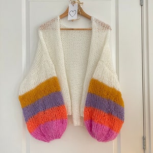 May include: White knit cardigan with long sleeves and a striped pattern in yellow, purple, orange, and pink on the sleeves.