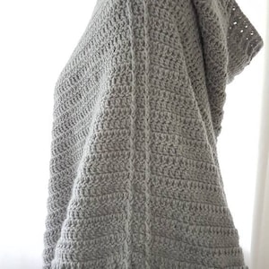K&ouml;nnte beinhalten: Ein graues, geh&auml;keltes Poncho mit Kapuze und einem strukturierten Stichmuster.