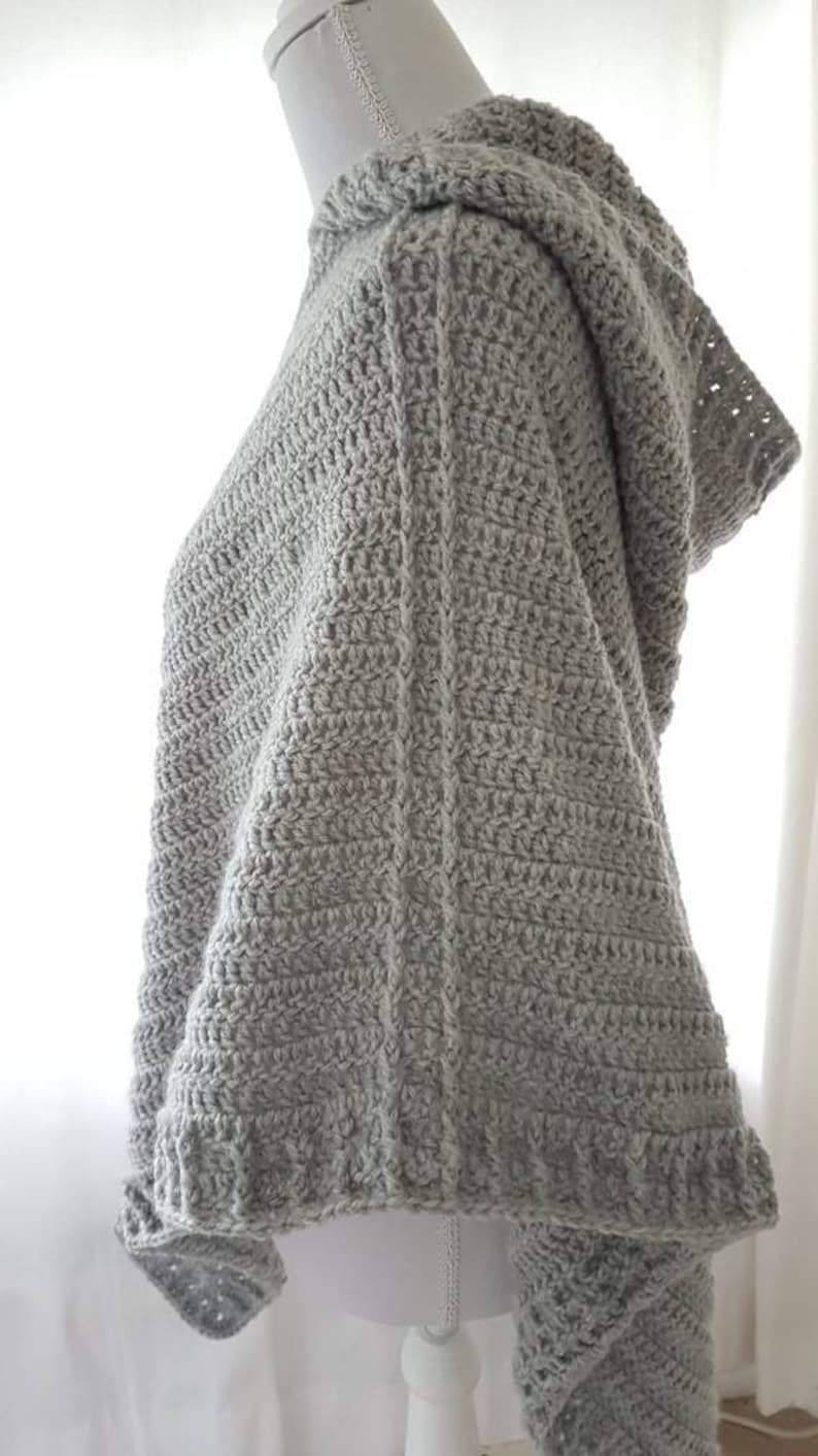 K&ouml;nnte beinhalten: Ein graues, geh&auml;keltes Poncho mit Kapuze und einem strukturierten Stichmuster.