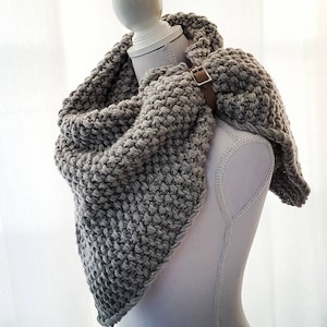 Op de afbeelding: Een grijze gebreide cowl met een bruin leren bandje. De cowl is over een wit mannequin gehangen.