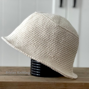 Op de afbeelding: Een gehaakte bucket hat in een licht beige kleur. De hoed heeft een brede rand en een eenvoudig ontwerp.