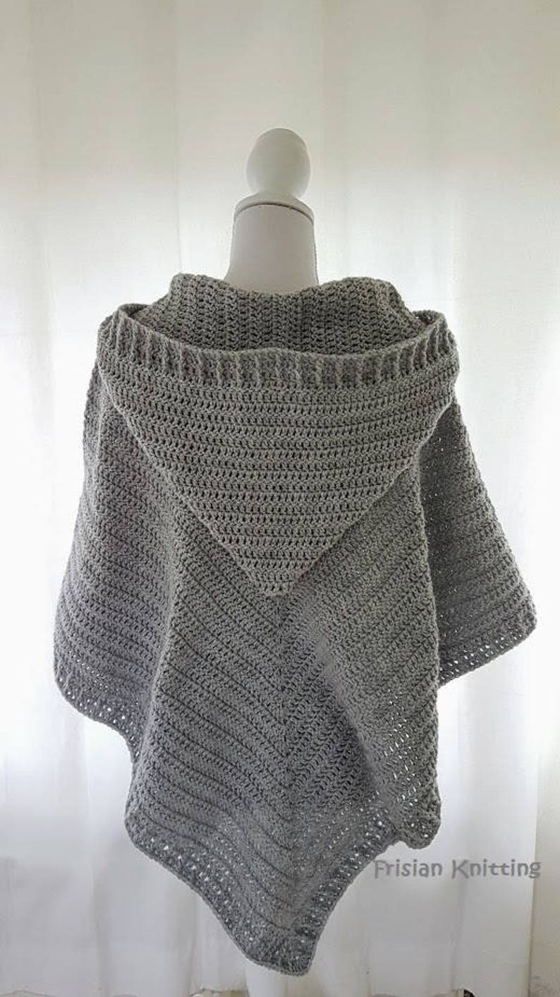 K&ouml;nnte beinhalten: Grauer geh&auml;kelter Kapuzenponcho mit dreieckiger Form und Fransenkante. Der Poncho wird auf einem wei&szlig;en Mannequin pr&auml;sentiert.